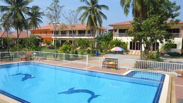 A swimming pool with dolphin designs, surrounded by palm trees and a building with balconies.
