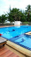 Piscina con azulejos de delfines, rodeada de palmeras y una valla blanca.