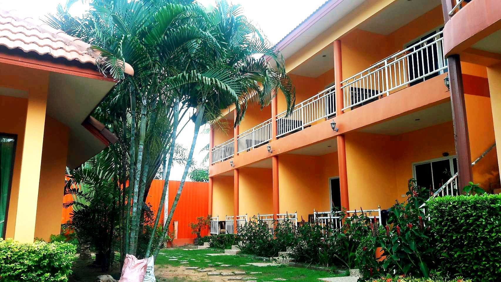 Un edificio de varios pisos con balcones, rodeado de abundante follaje y palmeras.