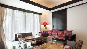 Un área de comedor con una mesa preparada para dos, un sofá con cojines a rayas, una lámpara roja y vistas al exterior a través de cortinas translúcidas.