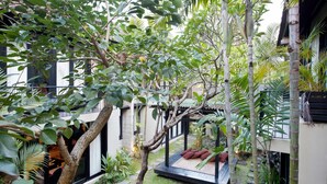 Un patio con banca de madera, abundante vegetación y un edificio tradicional.