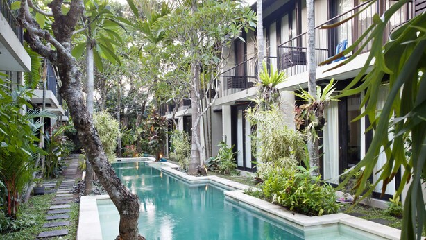 Zona de piscina con un camino accesible, rodeada de exuberante vegetación y edificios modernos con balcones.