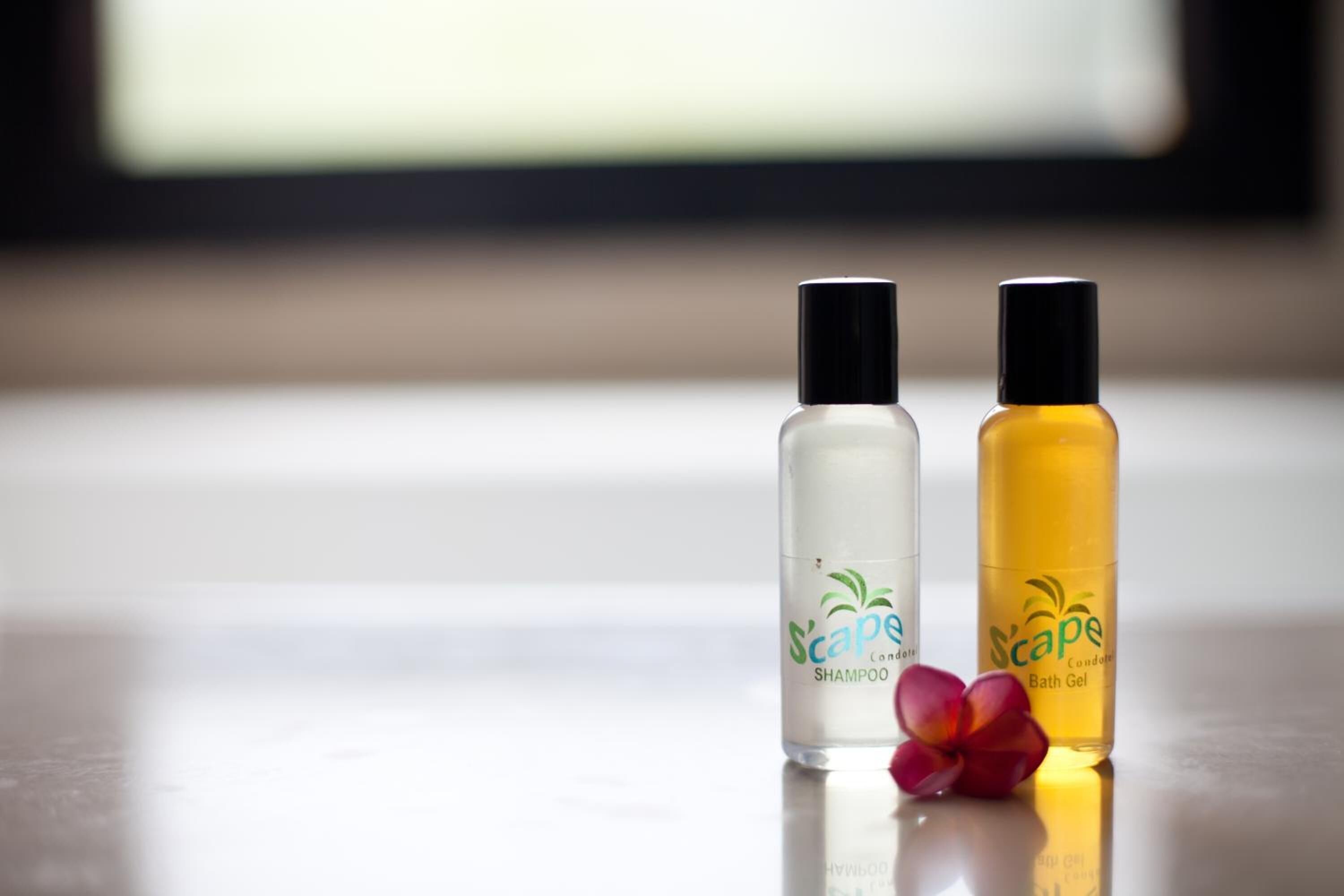 Deux bouteilles de shampoing et de gel douche de la marque « Scape », posées sur une surface réfléchissante, avec un arrière-plan flou.