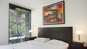 Habitación de hotel con cama, dos mesitas de noche, ventana con persianas y un cuadro abstracto colgado en la pared.