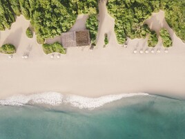 Vista aérea de una playa con una fila de sombrillas blancas y un edificio con techo tipo celosía.
