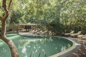 Un área de piscina con sillones de descanso y una estructura de techo de paja.