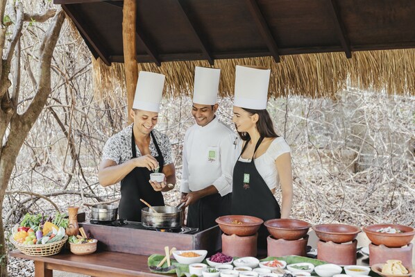 A group of chefs preparing food outdoors with cooking equipment and ingredients visible.