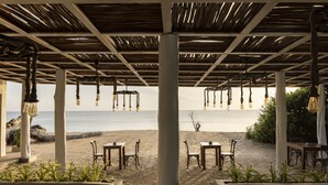 A beachside restaurant with outdoor seating, a thatched roof, and hanging light fixtures. - Jungle Beach an Uga Experience - Trincomalee (Kuchchaveli)