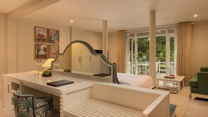 A hotel room with a bed, a desk with a mirror, a chair, and a small table with a lamp. - Jungle Beach an Uga Experience - Trincomalee (Kuchchaveli)