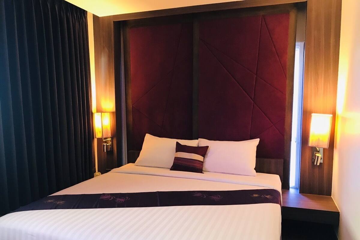 A hotel room with a large bed, dark curtains, and two wall-mounted lamps.
