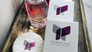 A wooden tray with a shower gel bottle, a bottle of perfume, and two sanitary bags with the Paradise Boutique Suites logo. - Paradiso Boutique Suites (Bangkok)