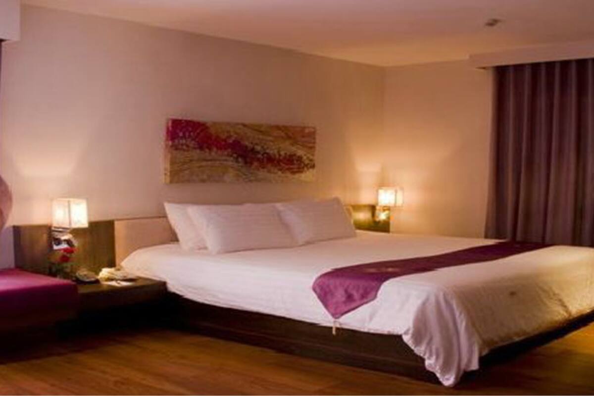 A hotel room with a large bed, two bedside lamps, a nightstand, a window with curtains, and a wall-mounted artwork.