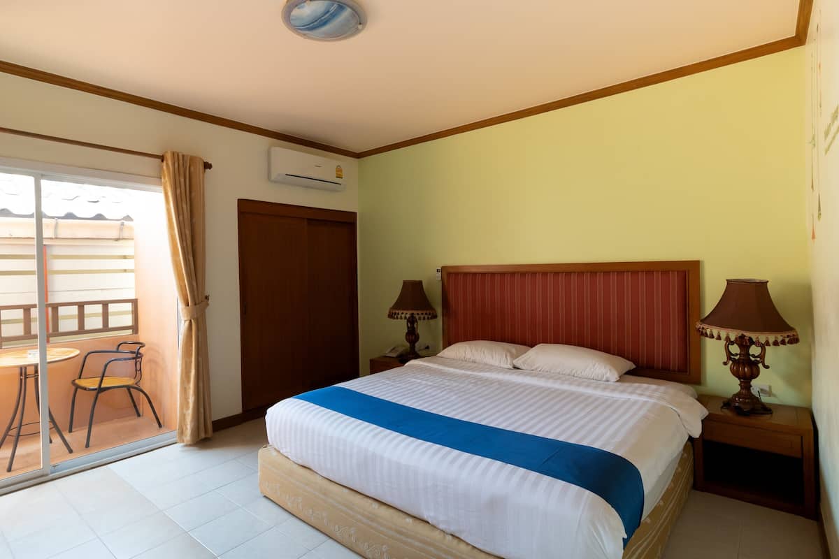 Quarto de hotel com cama, duas luminárias de cabeceira, janela com cortinas, uma mesinha com cadeira e um aparelho de ar condicionado.