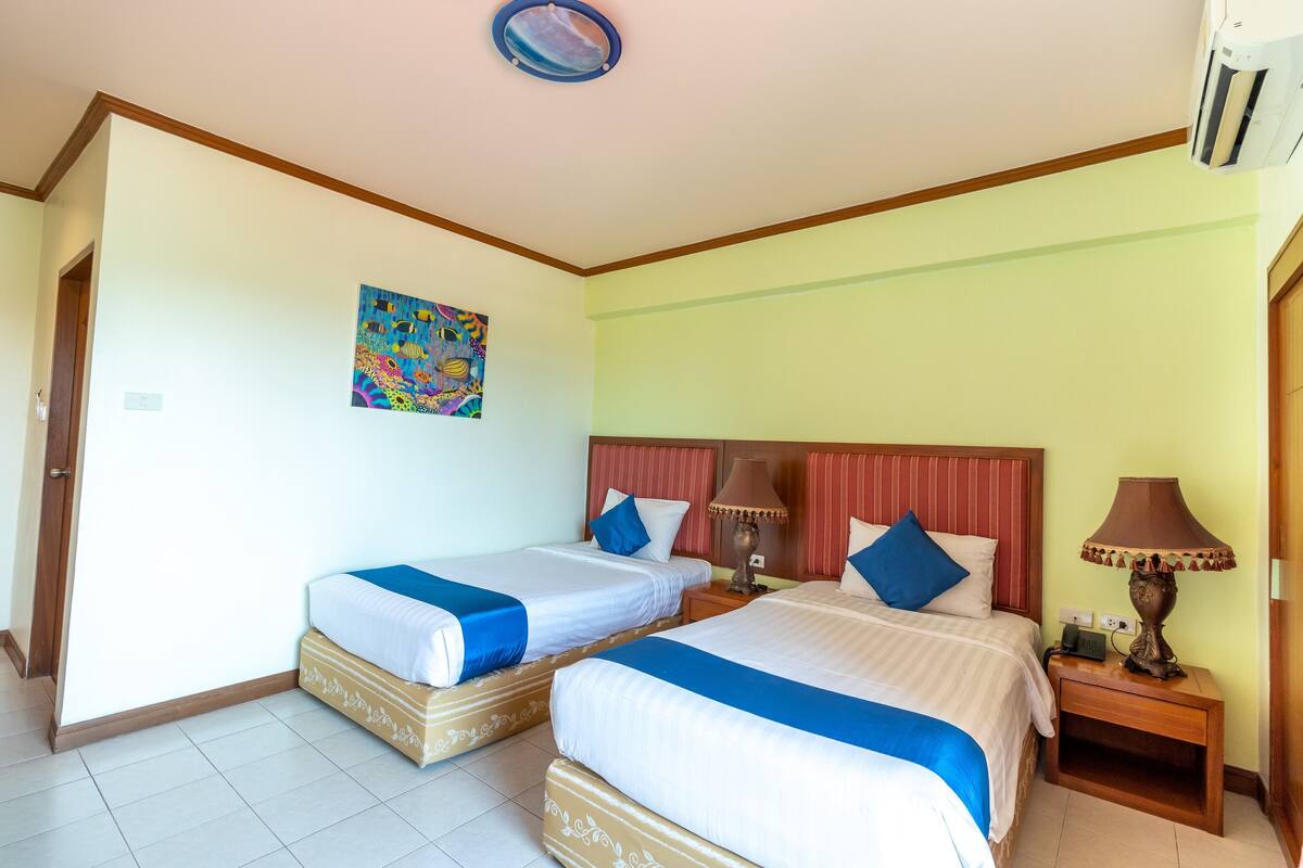 Quarto de hotel com duas camas, um quadro na parede e uma mesa de cabeceira com abajur.