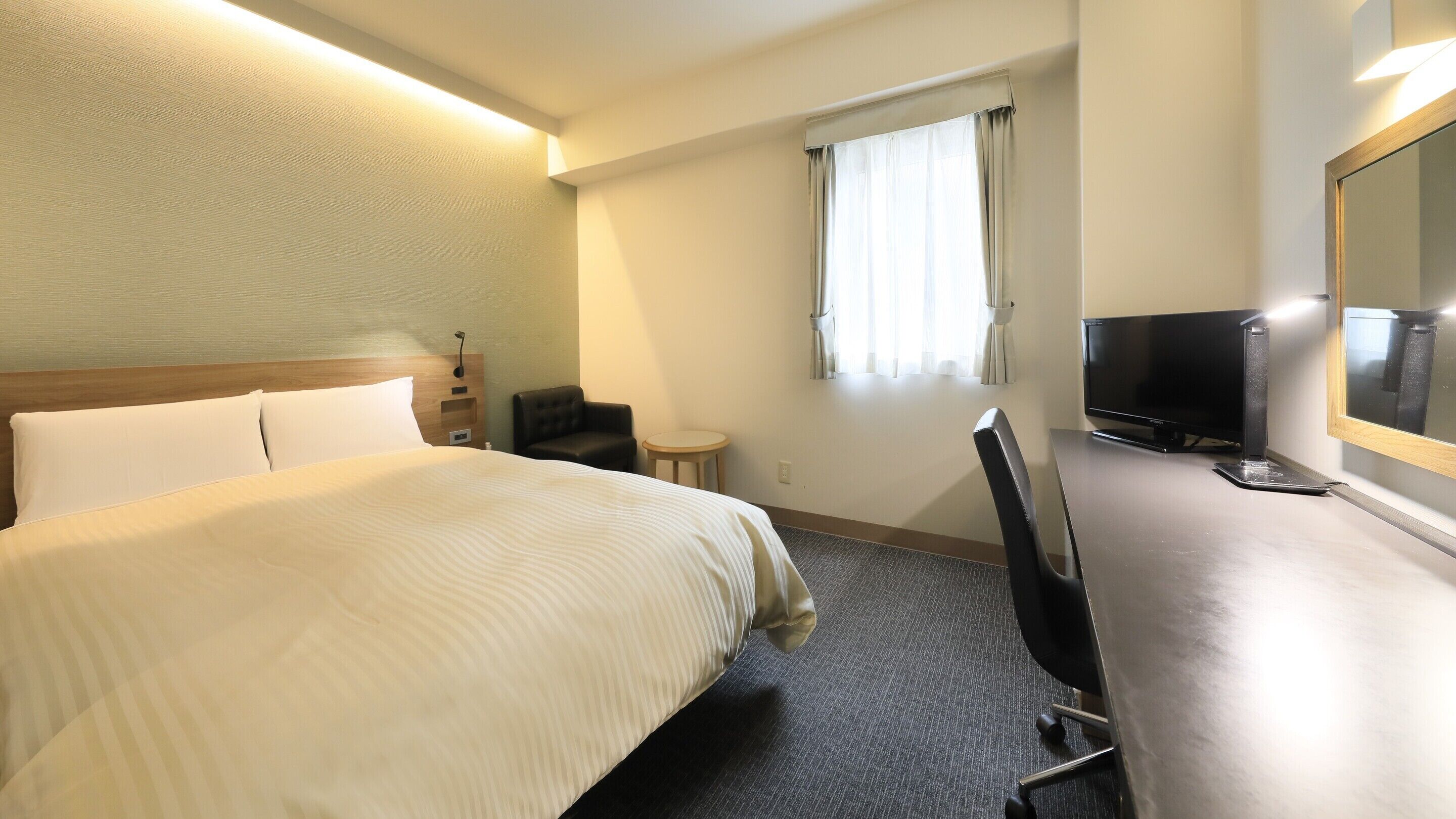 A hotel room with a large bed, a desk with a chair, a television, and a window with curtains.