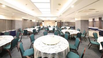 Un salón de banquetes con mesas redondas y sillas, un escenario y una larga barra.