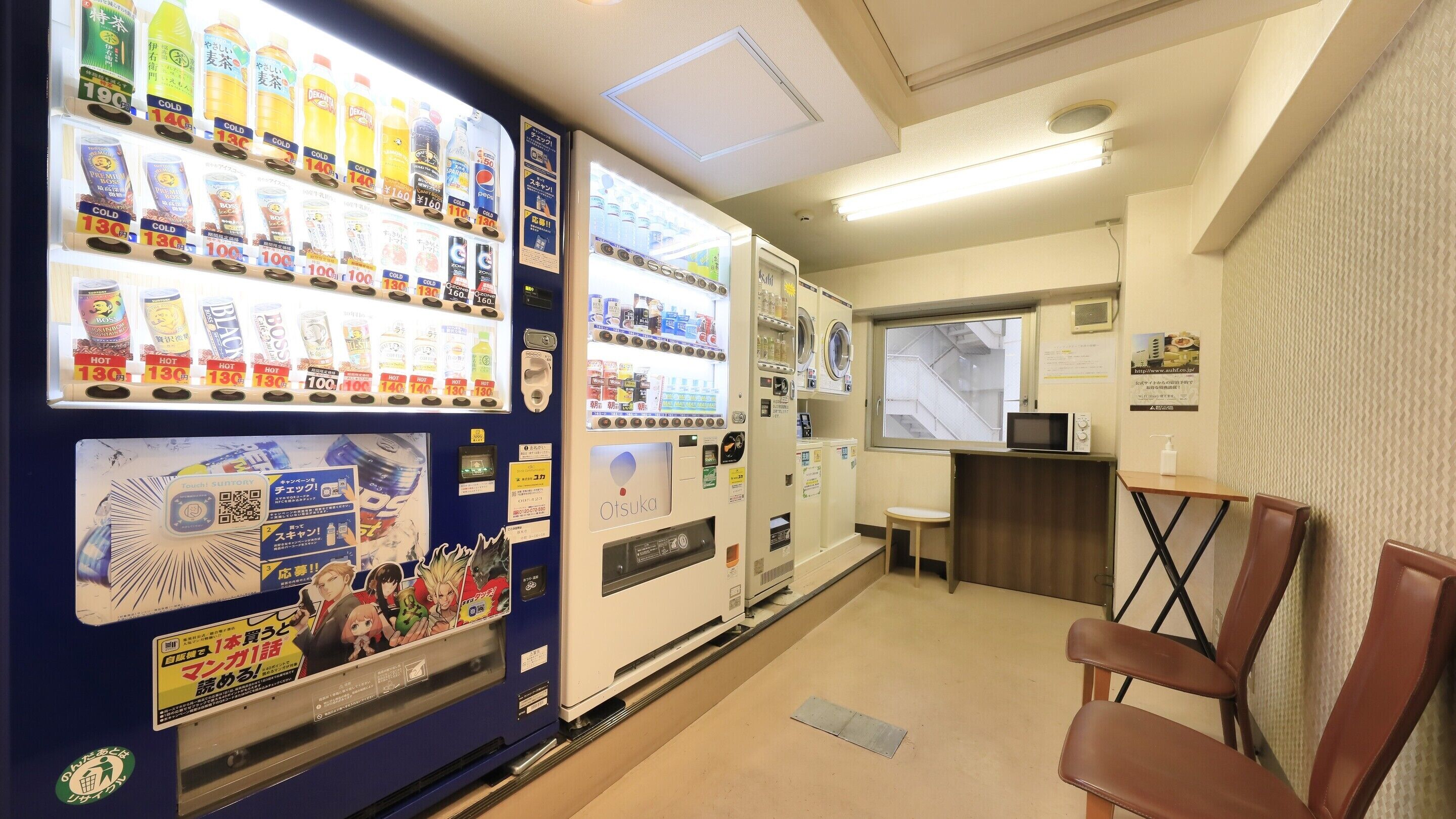 Un espace équipé d’un distributeur automatique proposant diverses boissons et collations, d’un four à micro-ondes et d’un petit coin salon avec une chaise.