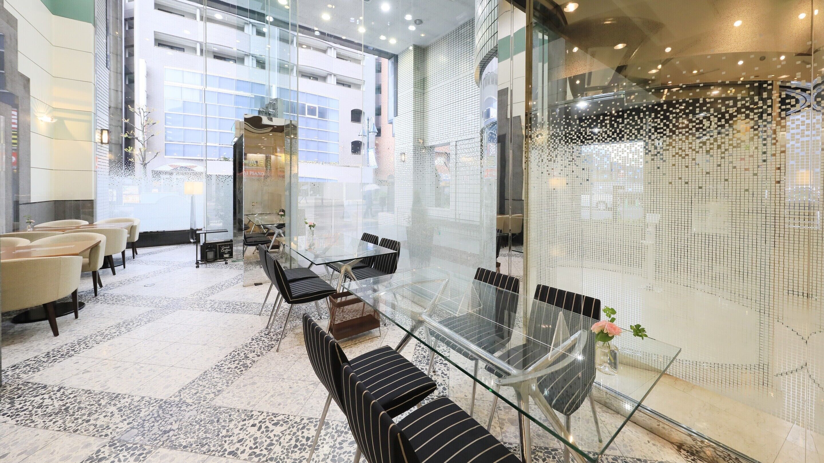A modern hotel lobby with a glass partition, seating area with chairs and tables, and a piano.