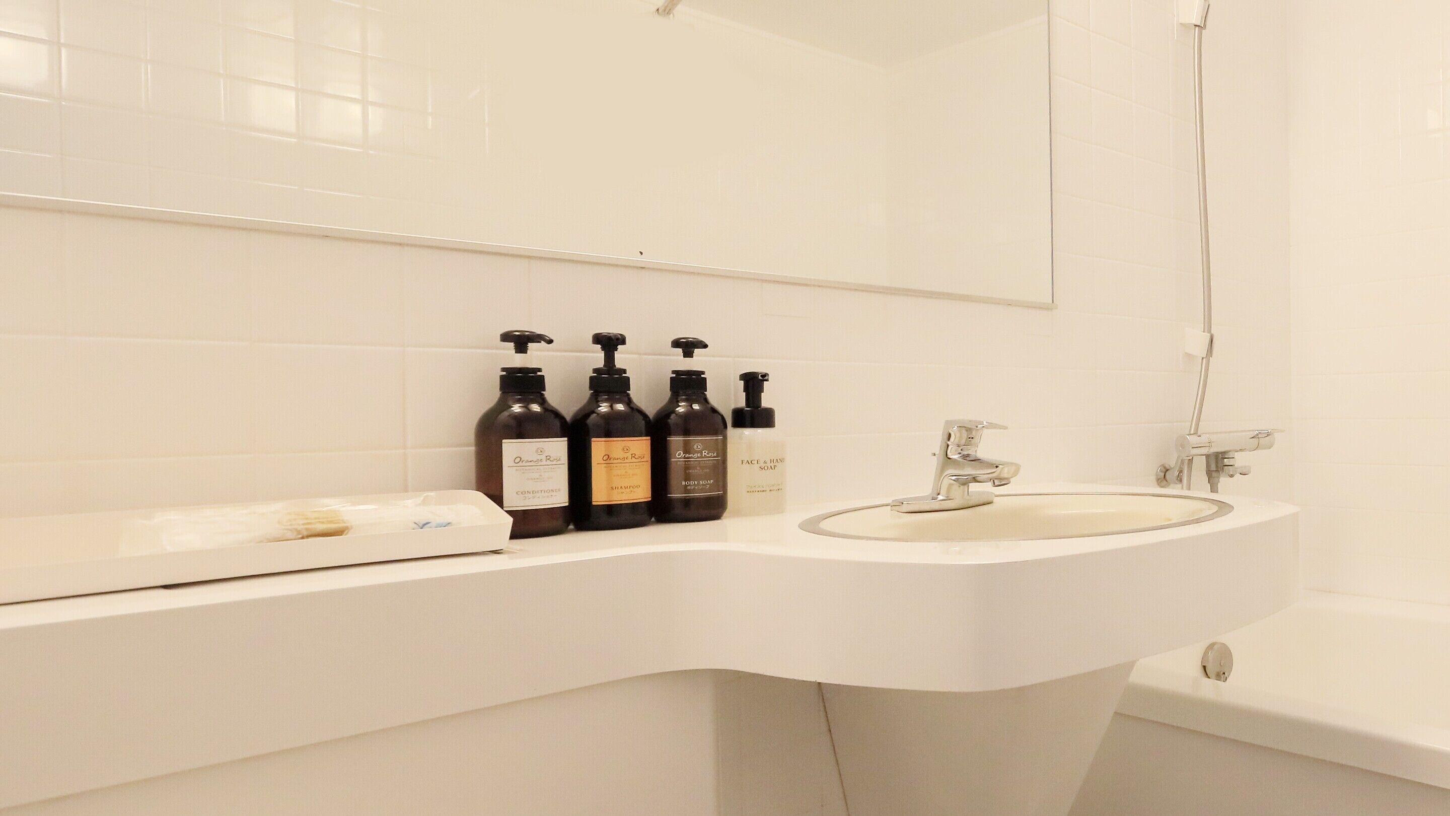 A bathroom with a white sink, a mirror, and three bottles of Orange Rose products.