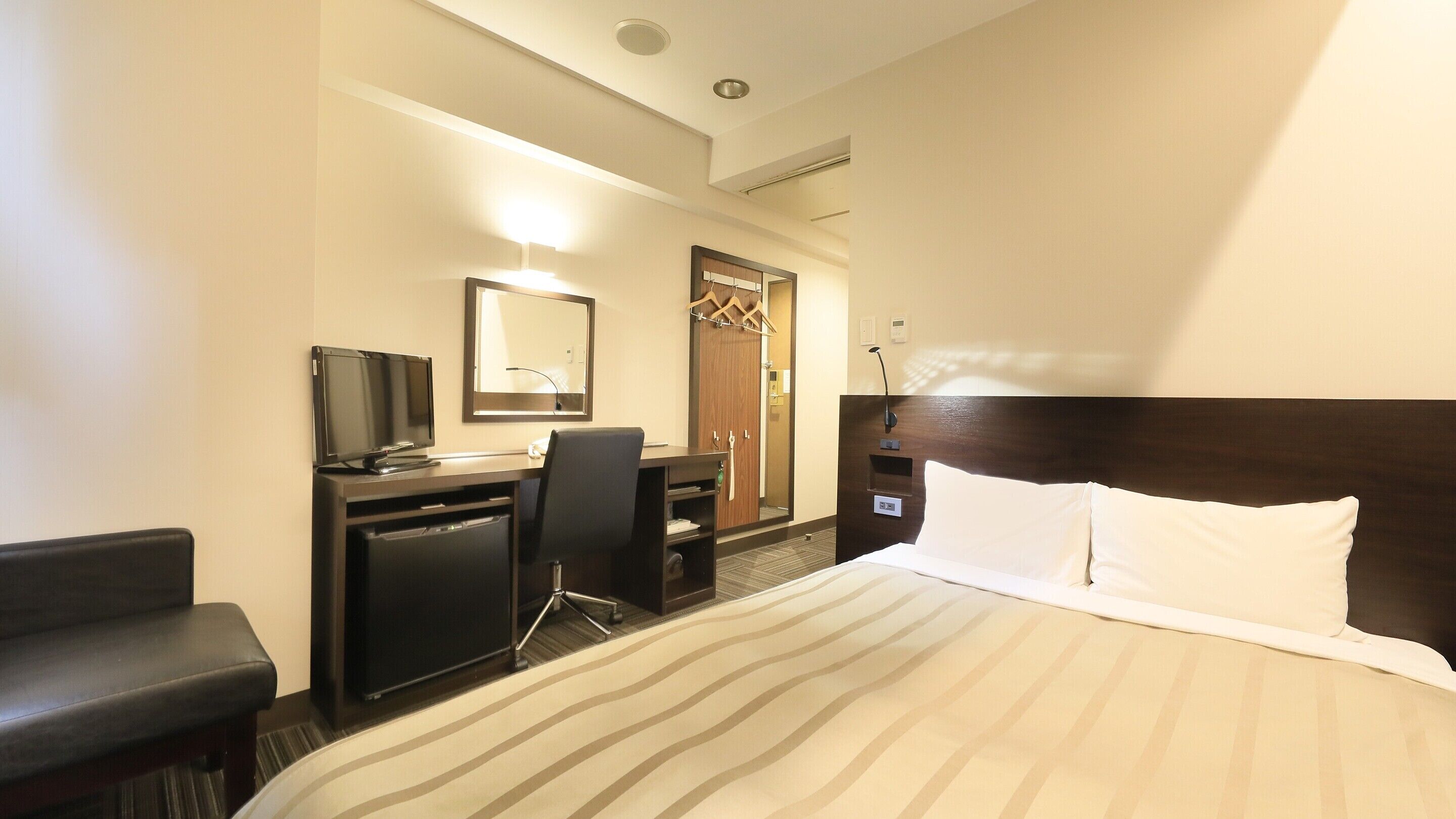 Una habitación de hotel con una cama, un escritorio con ordenador, una silla, televisión y espejo.