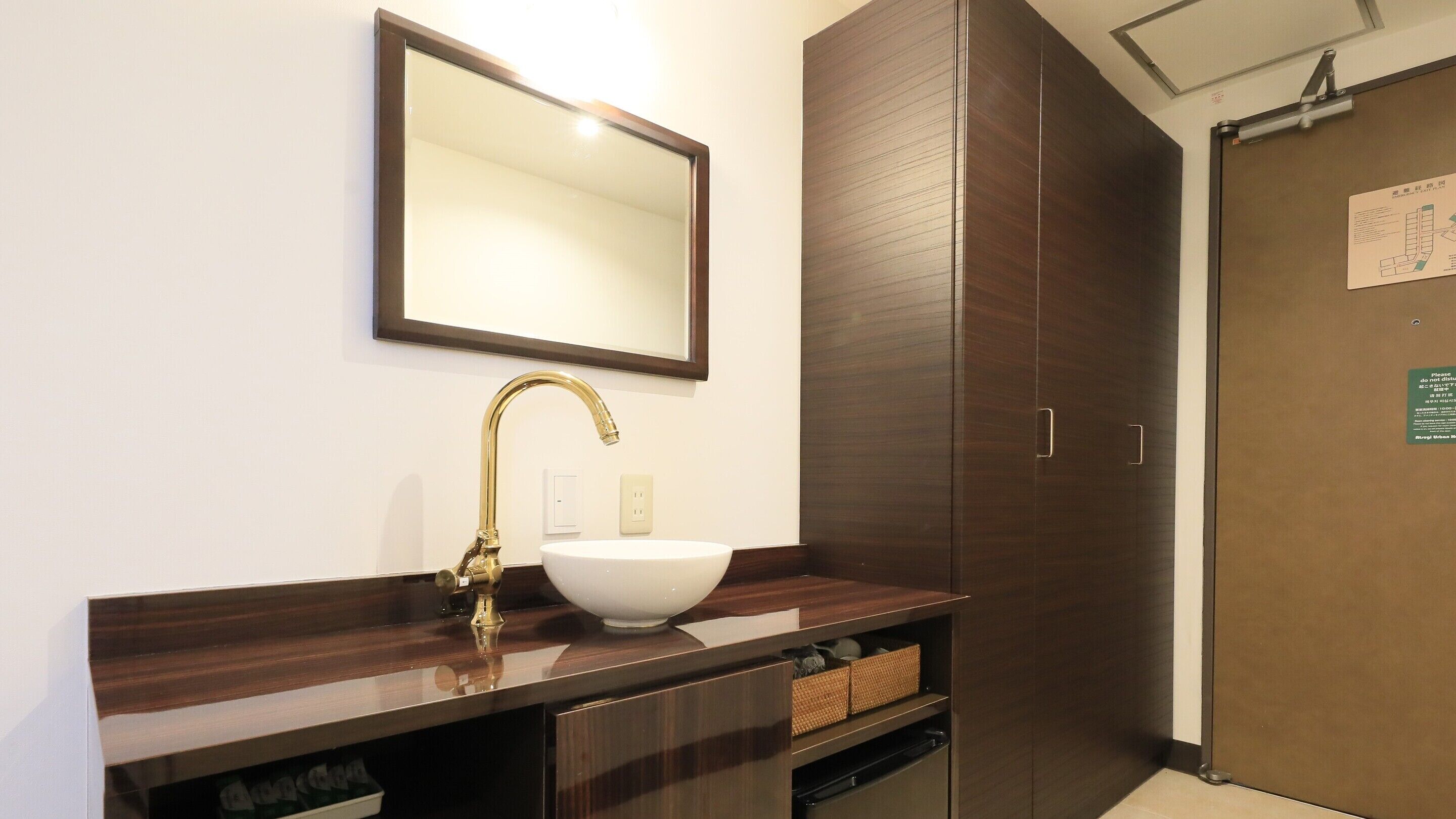 A bathroom with a white sink, gold faucet, and a mirror above it. There is a wooden cabinet below the sink and a door to the right.