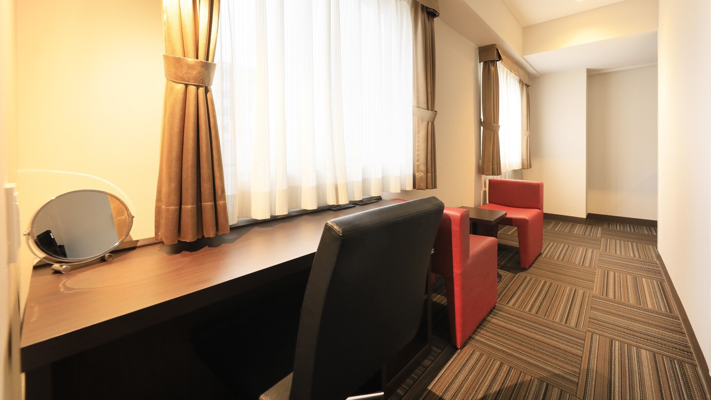A hotel room with a desk, two chairs, a small table, and a mirror.