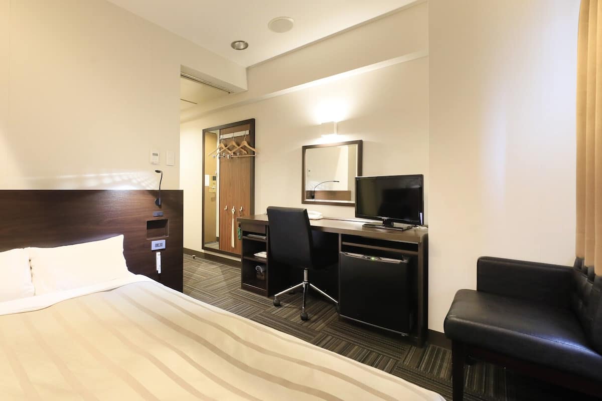 Ein Hotelzimmer mit einem Bett, einem Schreibtisch mit Computer, einem Fernseher und einem Sessel.