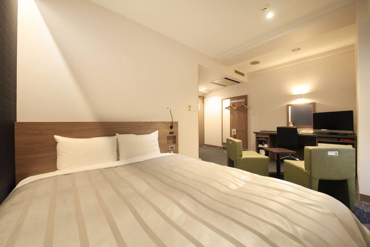 Ein Hotelzimmer mit einem großen Bett, einem Schreibtisch mit Computer, einem Stuhl und einem Spiegel.