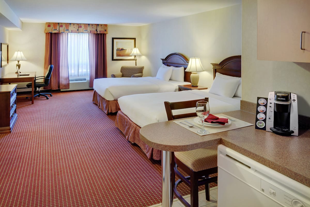 A hotel room with two beds, a desk, a chair, a coffee maker, and a dining table.