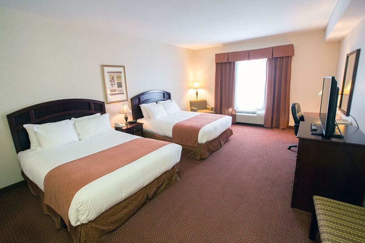 A hotel room with two beds, a desk, a chair, a TV, and a window with curtains.
