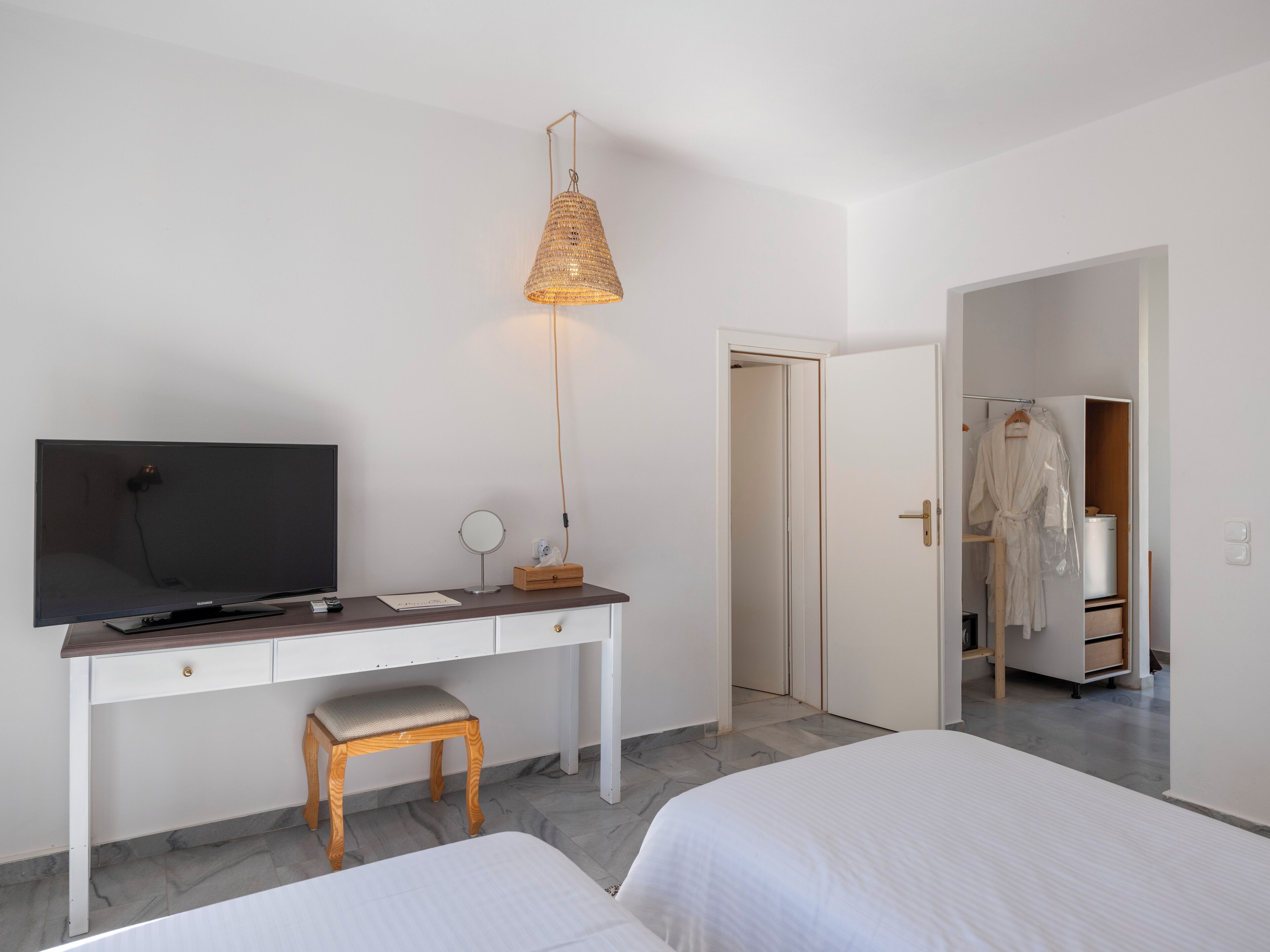 Une chambre d’hôtel avec un lit, un bureau avec une télévision, un miroir et un peignoir accroché à la porte.