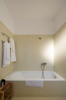 A bathroom with a bathtub, a towel rack with towels, and a small wooden stool.