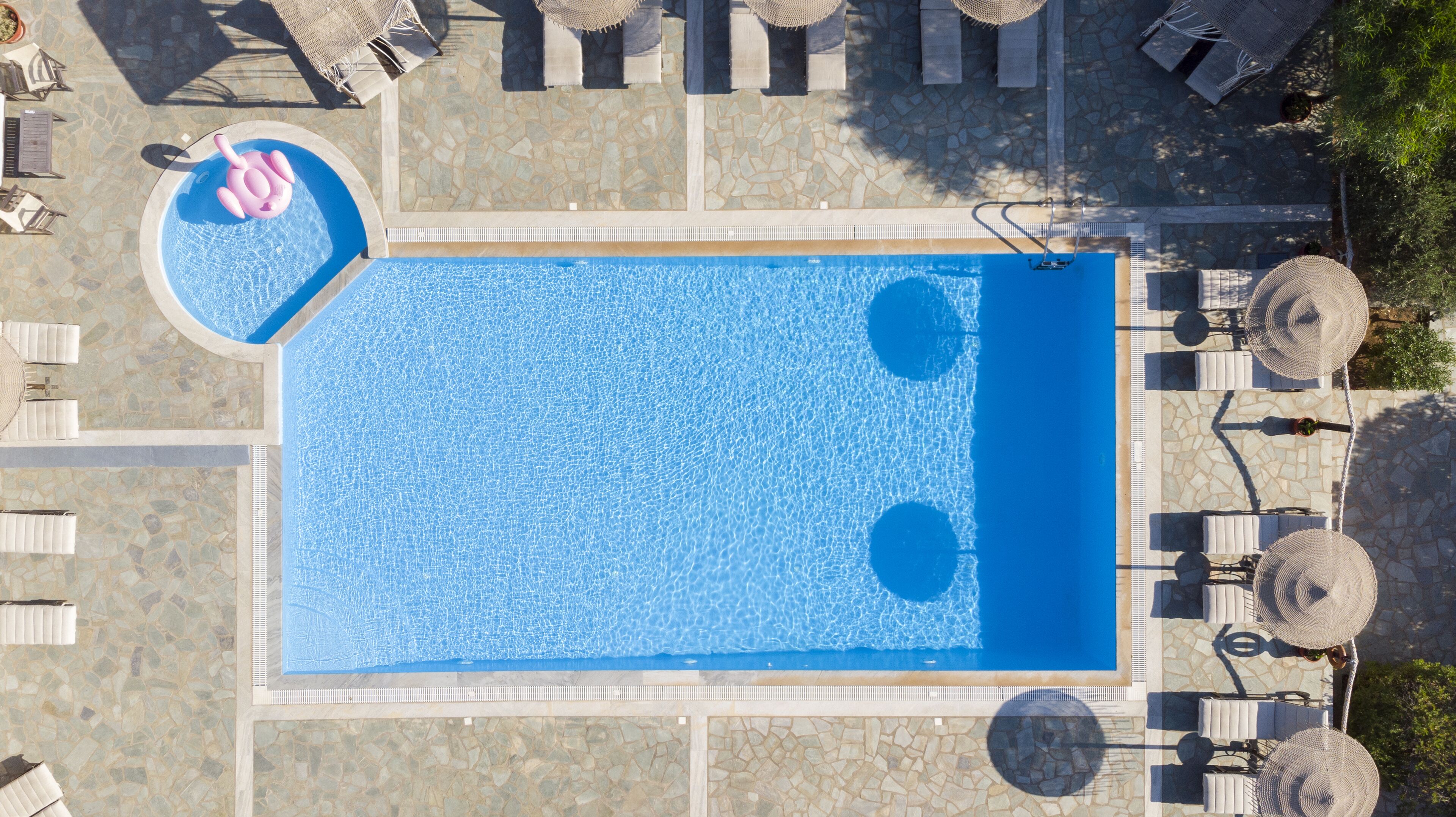 An aerial view of a rectangular swimming pool with a small circular section, surrounded by lounge chairs and umbrellas.