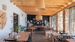 A restaurant with wooden tables and chairs, a stone floor, and a black wall with decorative plates. - Parosland Hotel (Paros)