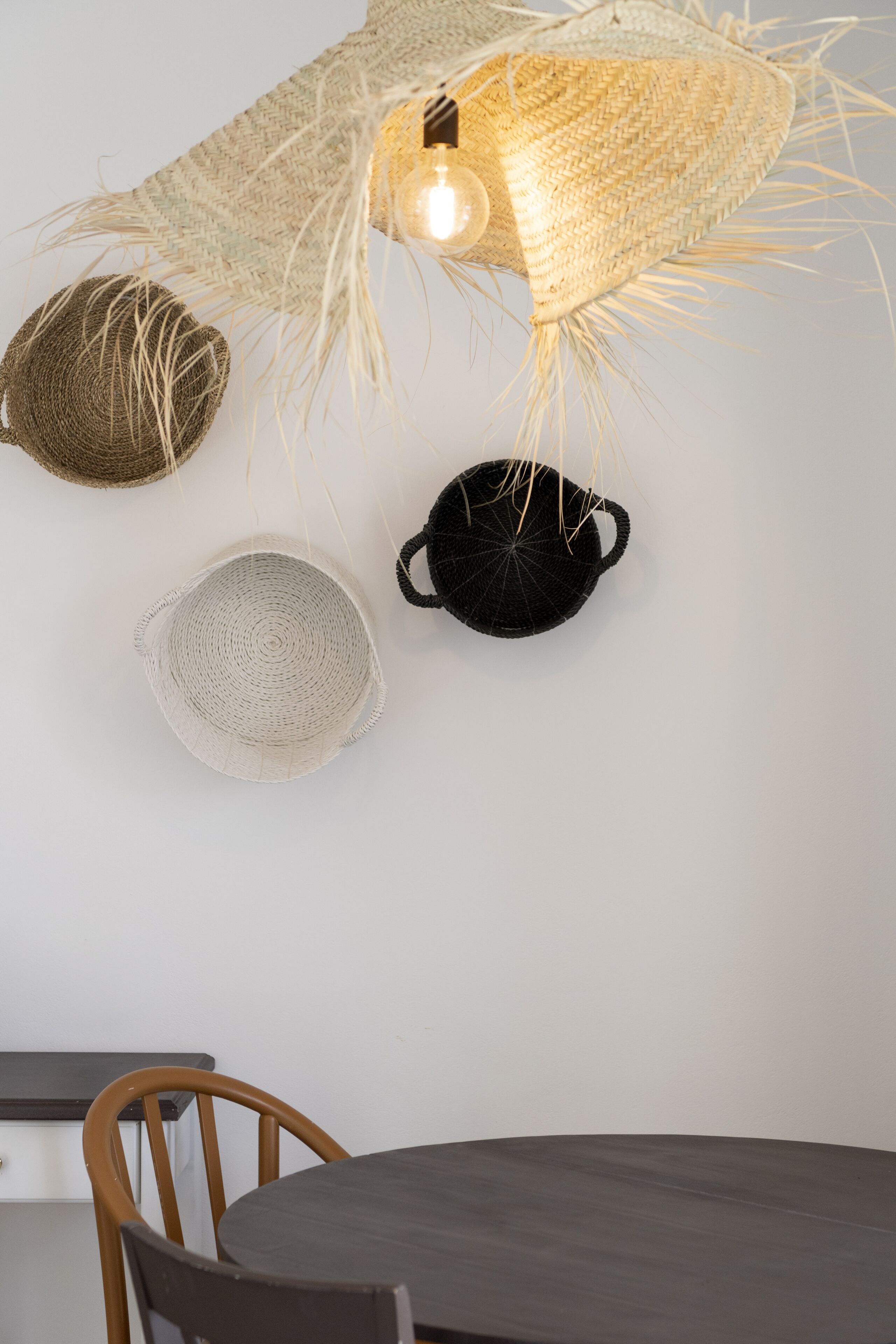 A dining area with a round table, a chair, and a woven ceiling light fixture.