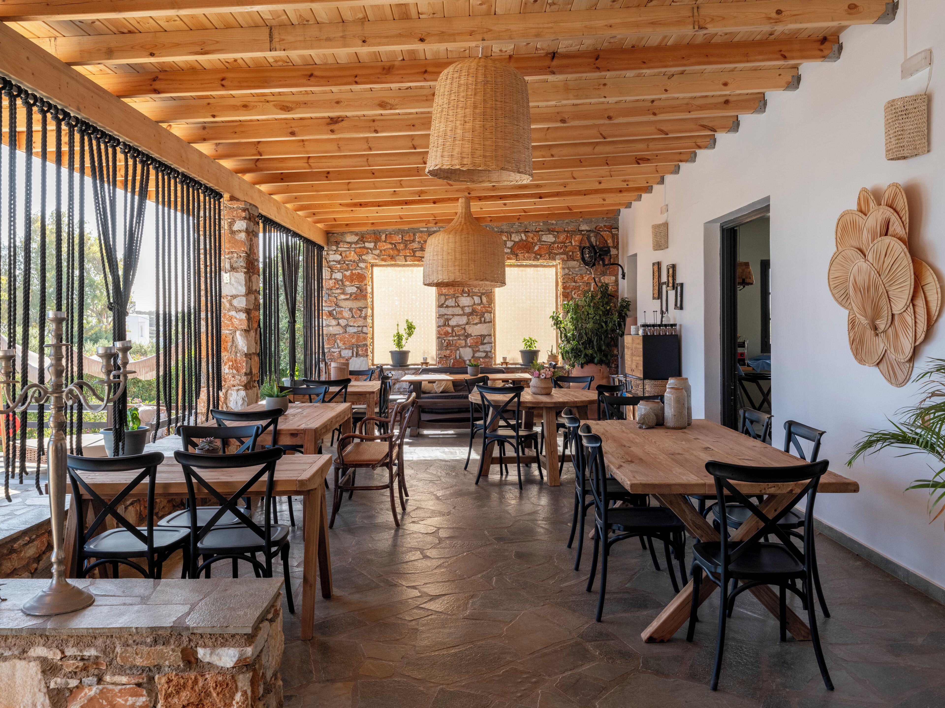 A spacious patio area with wooden tables and chairs, stone flooring, and a stone wall.