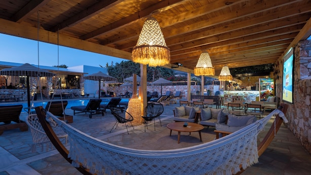 A cozy outdoor seating area with a hammock, lounge chairs, and a pool. - Parosland Hotel (Paros)