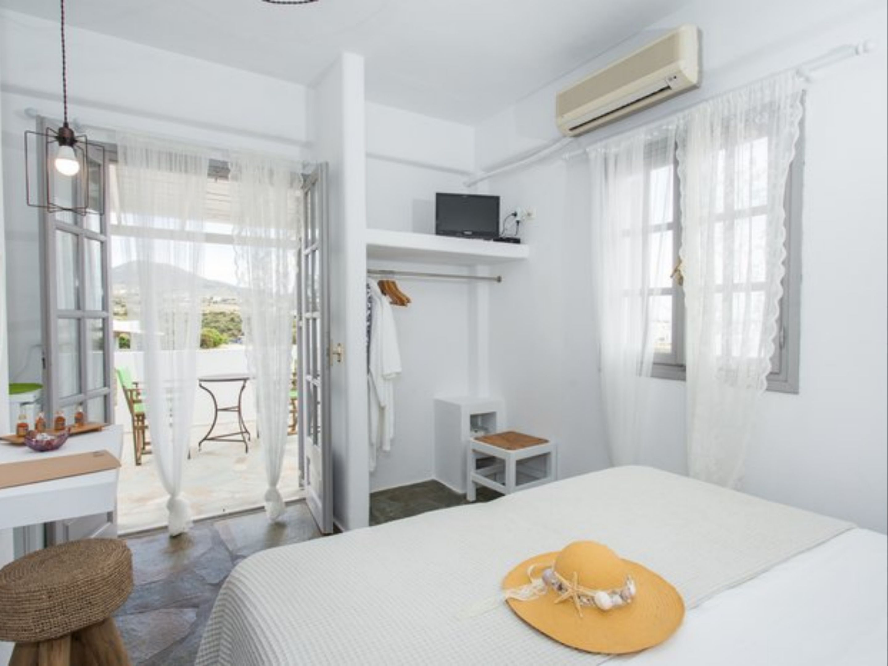 A bedroom with a bed, a TV, a desk, and a chair. There is a balcony with a table and chairs.