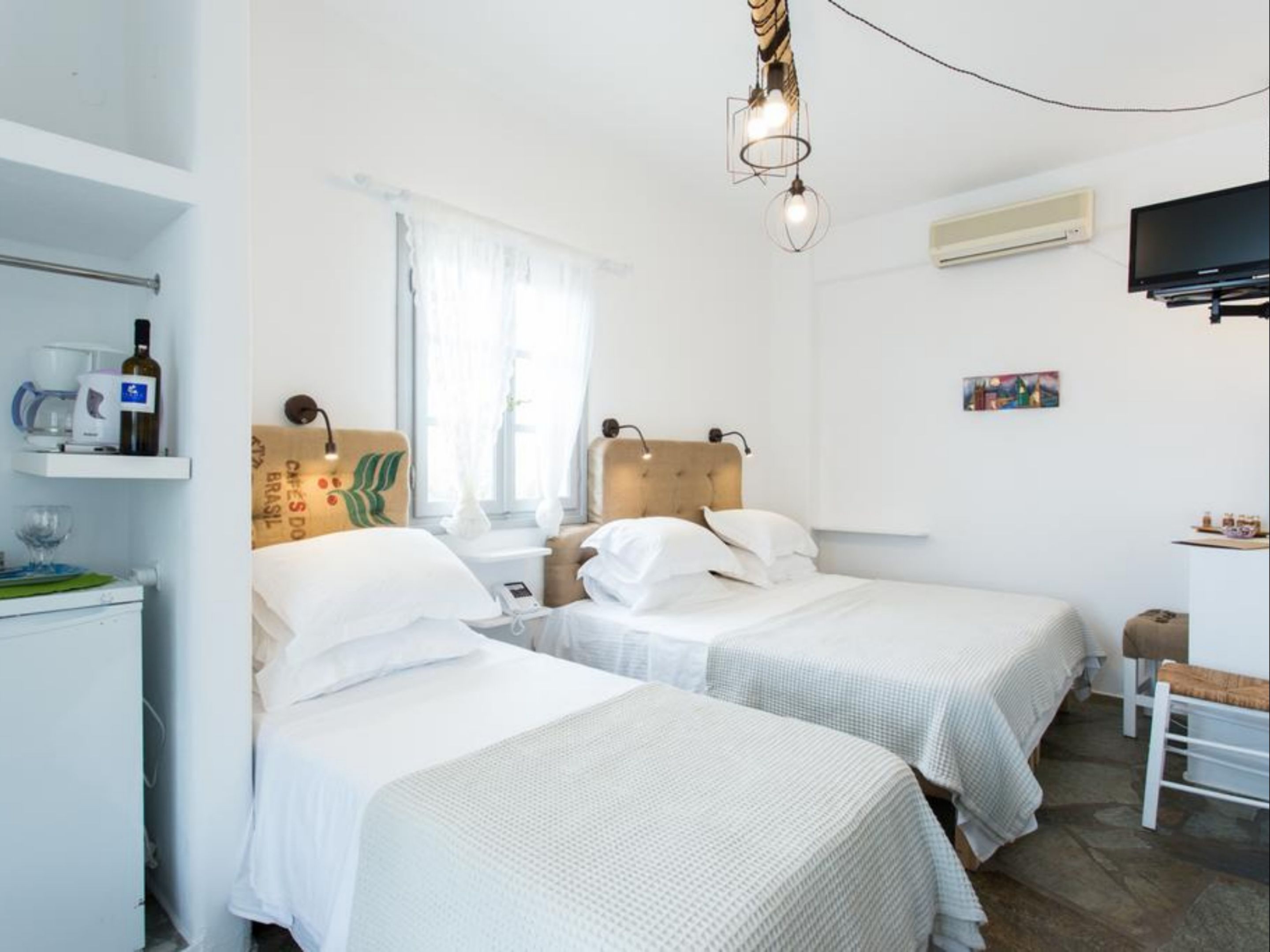 A hotel room with two beds, a small table, a chair, a TV, and a window with curtains.