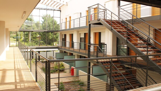 Een meerlaags interieur met een centrale trap, houten vloeren en metalen balustrades.