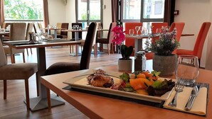 Een eetgedeelte met gedekte tafels voor een maaltijd, inclusief een bord met geroosterd vlees en groenten.