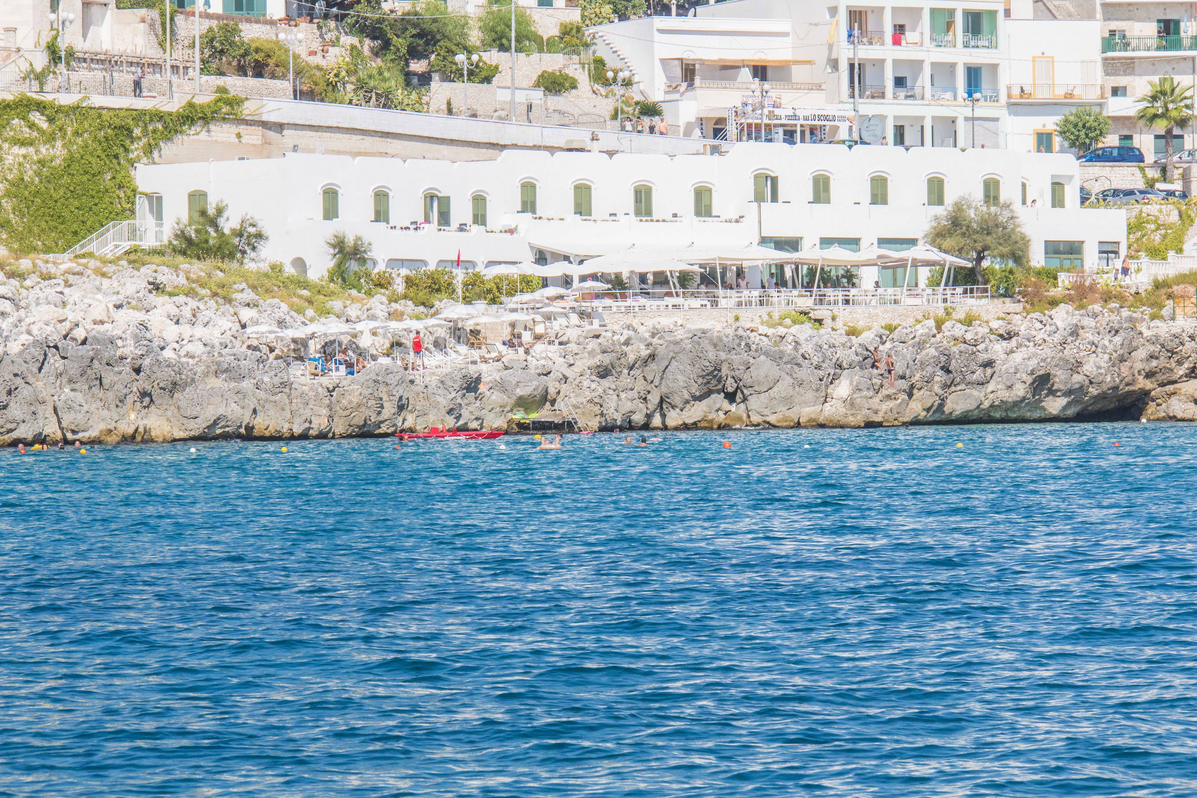 Un hôtel situé sur la côte, composé de plusieurs bâtiments blancs, avec un rivage rocheux et une mer d’un bleu limpide.
