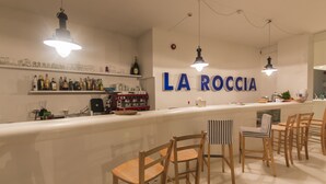 A bar area with a counter, wooden chairs, and a wall with 'LA ROCCIA' signage.