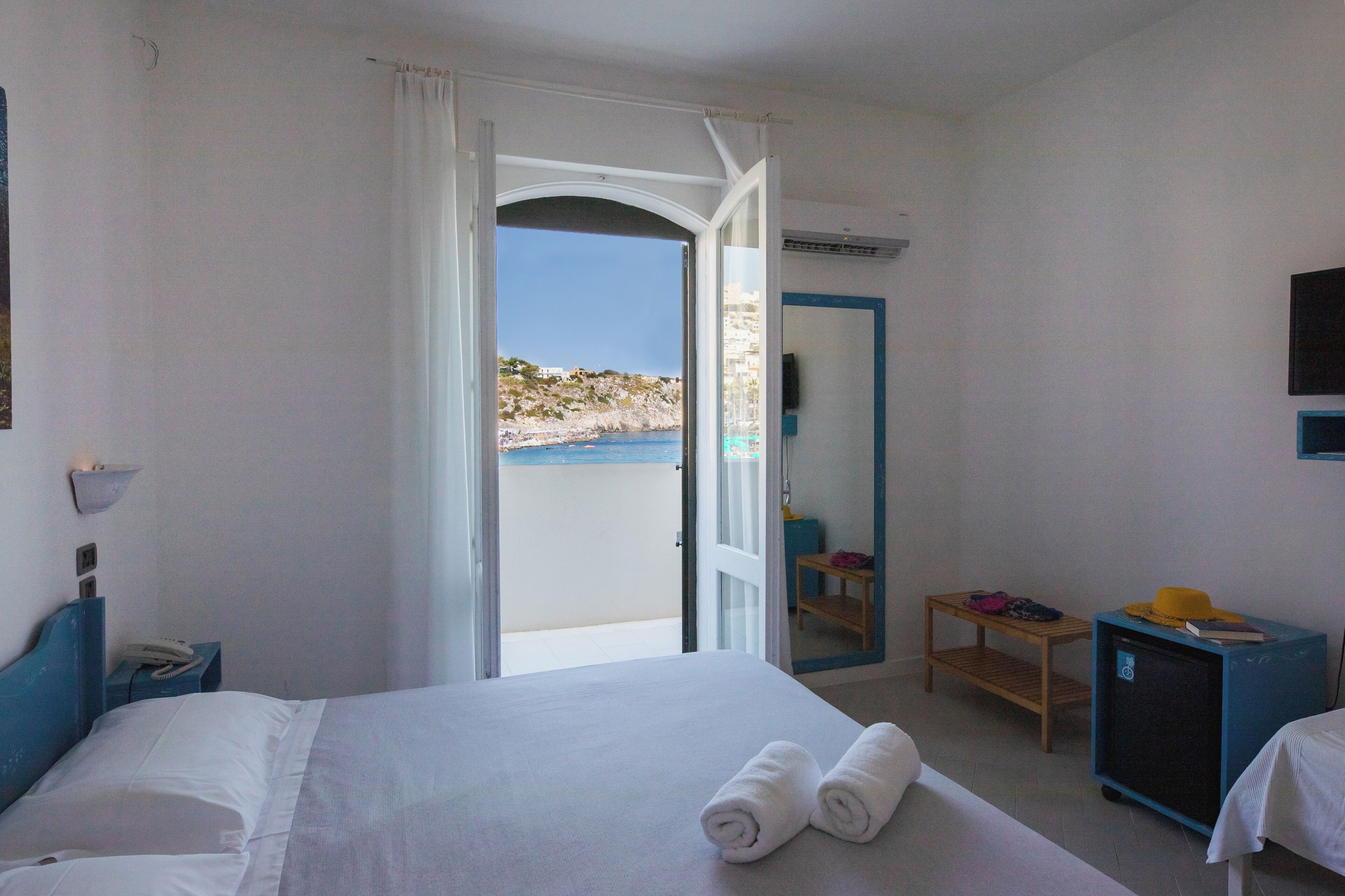 Habitación de hotel con cama, escritorio, silla, pequeña mesa, armario y vista al mar.