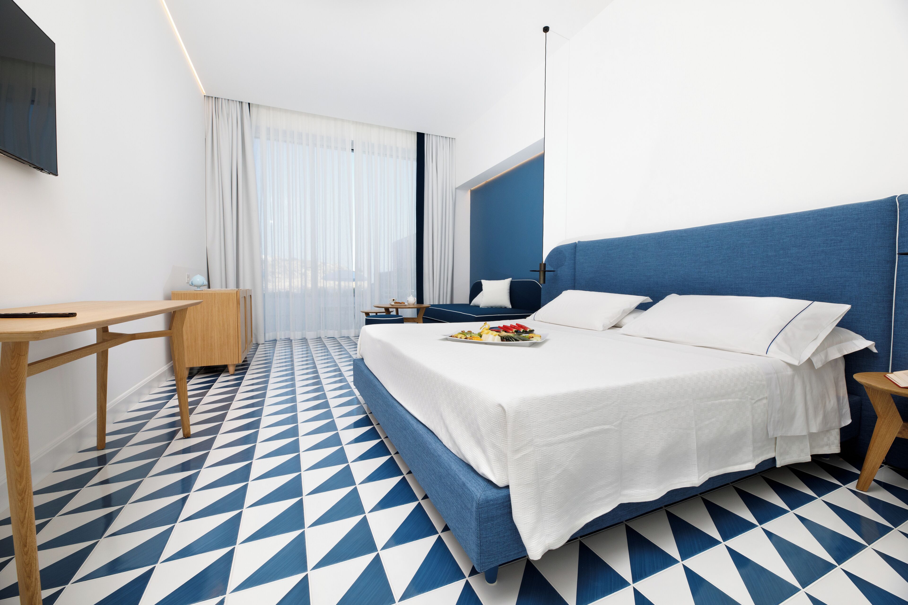 A modern hotel room with a large bed, a desk, and a TV.