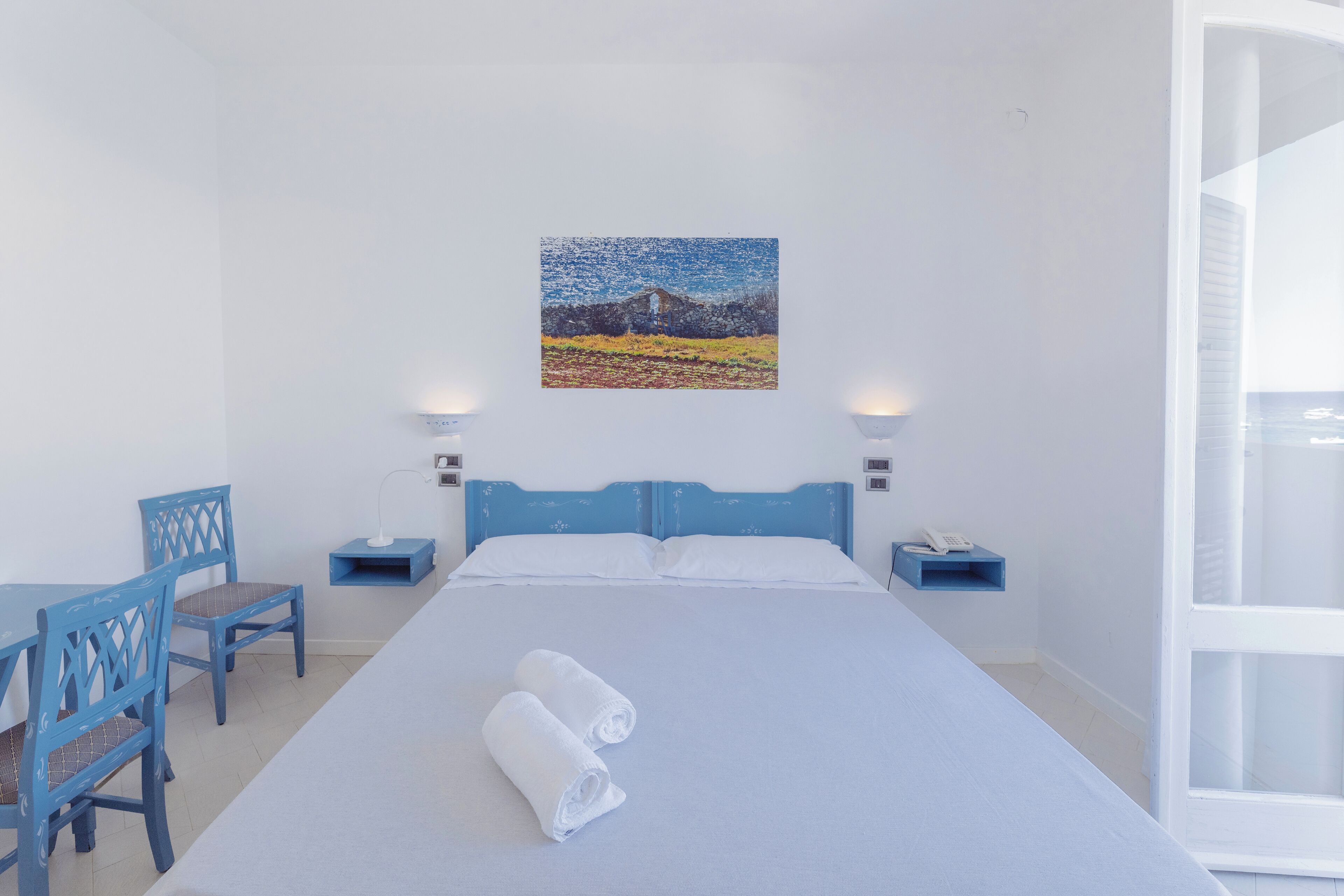 Ein Hotelzimmer mit einem Bett, zwei Nachttischen, einem Schreibtisch mit Stuhl und einem Bild an der Wand.