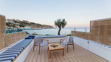 Una terraza con asientos, una mesa y vistas al mar y las colinas.