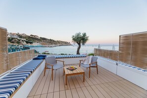 A deck with seating, a table, and a view of the sea and hills.