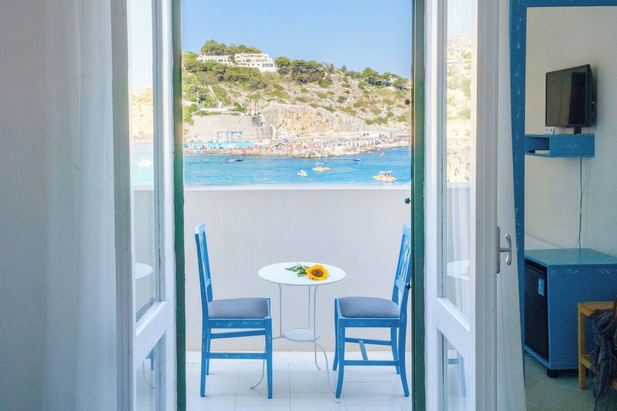 A balcony with two blue chairs and a small table with a sunflower.
