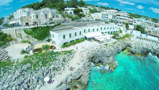 A coastal hotel with multiple floors, outdoor seating, and a rocky shoreline.